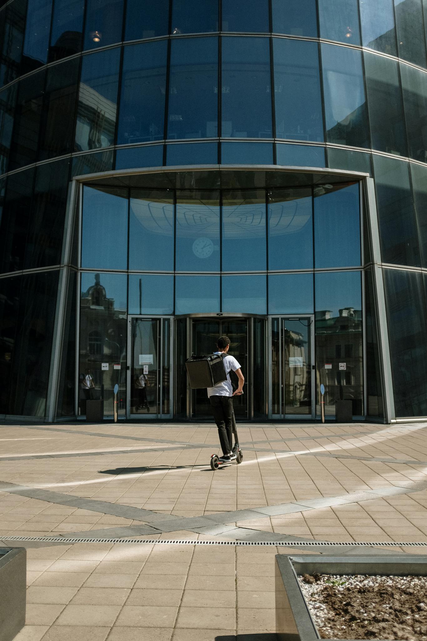 Man in White Shirt and Black Pants Riding on Black Skateboard in Front of Glass Building